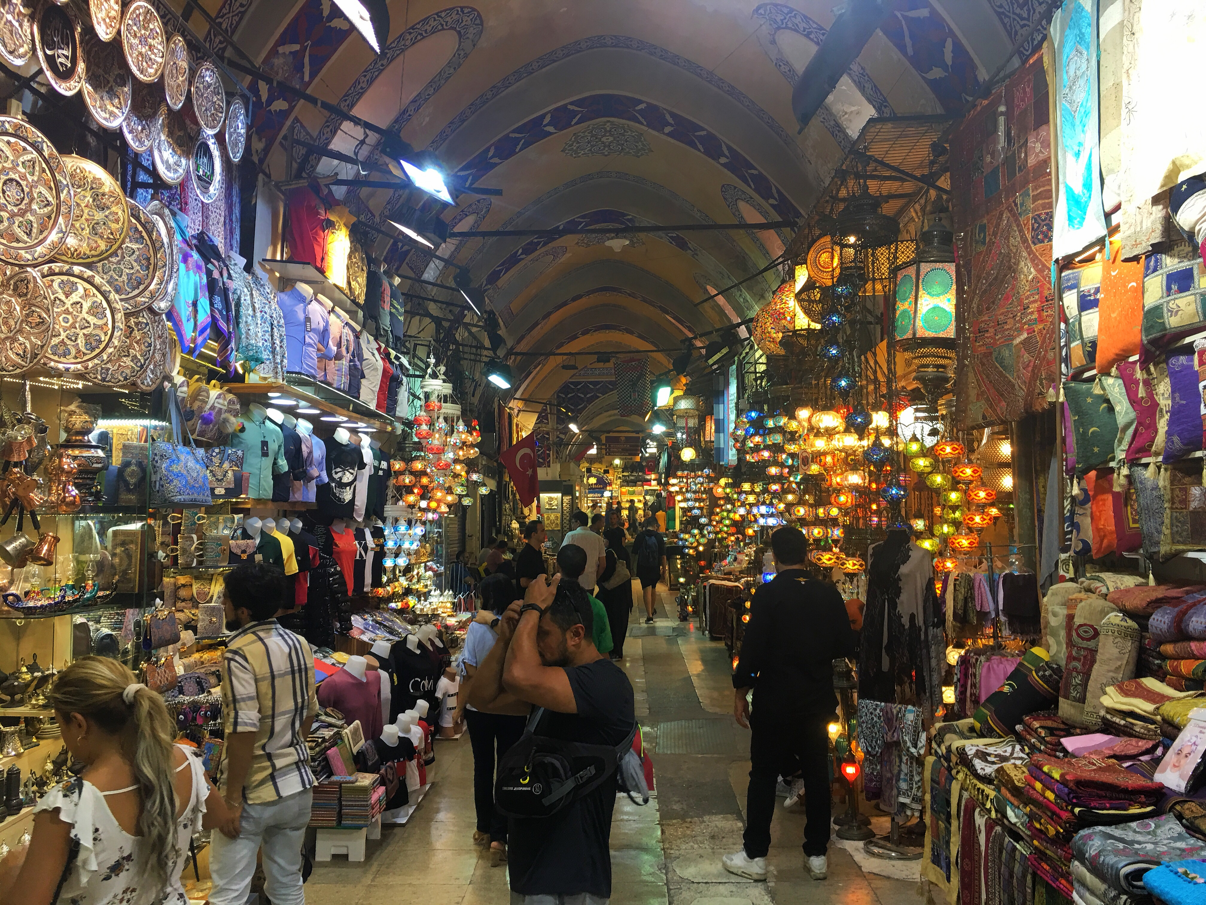 Orientalischer Markt mit vielen Ständen, die unterschiedliche Waren anbieten. Zu sehen sind unter anderem Kleidung, Dekobeleuchtung sowie Kunsthandwerk. Mehrere Menschen schauen die Waren an. Orientalischer Markt mit vielen Ständen, die unterschiedliche Waren anbieten. Zu sehen sind unter anderem Kleidung, Dekobeleuchtung sowie Kunsthandwerk. Mehrere Menschen schauen die Waren an.